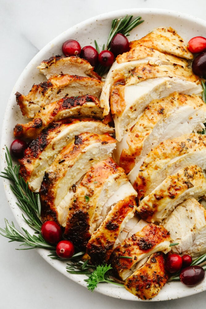 This juicy air fryer turkey is SOO GOOD and will have all of your guests asking for more! It's perfectly golden brown and dripping in flavor... You will never cook a turkey any other way again! Sliced turkey on a plate with garnish.