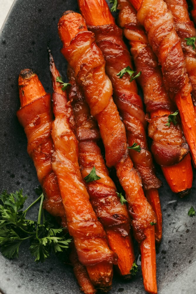 Wow, your guests this holiday season with these amazing bacon-wrapped, honey-glazed carrots! They're saucy and tender with the perfect mix of sweet and savory! Baked bacon-wrapped carrots garnished with parsley.