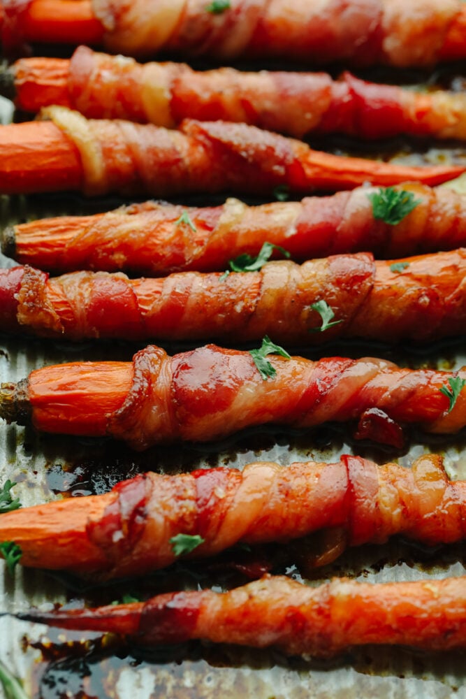 Wow, your guests this holiday season with these amazing bacon-wrapped, honey-glazed carrots! They're saucy and tender with the perfect mix of sweet and savory! Closeup of bacon-wrapped, honey-glazed carrots garnished with parsley.