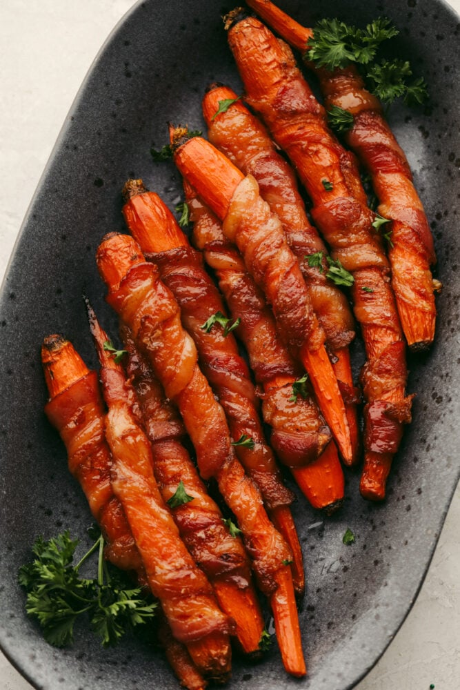 Wow, your guests this holiday season with these amazing bacon-wrapped, honey-glazed carrots! They're saucy and tender with the perfect mix of sweet and savory! Bacon-wrapped carrots in a stoneware serving dish.
