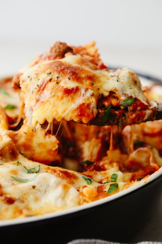 This baked ravioli is a knockout dinner that is sure to be loved by all! It's smothered in melty mozzarella, parmesan, and a tasty meat sauce! Scooping up ravioli with a wooden spoon.