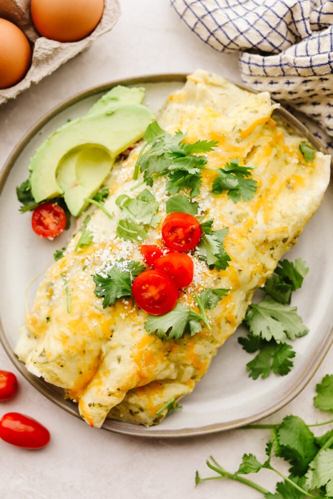My easy breakfast enchiladas are packed with sausage, fluffy eggs, and zesty salsa, then smothered in a rich, creamy sauce that puts every other breakfast to shame. You can even make them ahead! A plate with breakfast enchiladas garnished with cilantro, avocado and tomatoes.