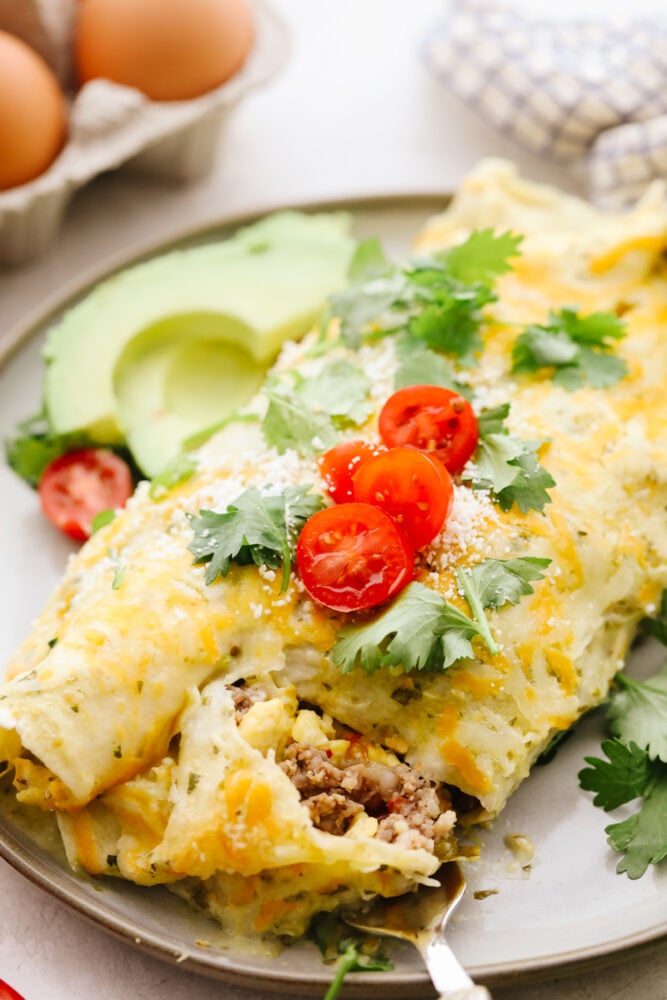 My easy breakfast enchiladas are packed with sausage, fluffy eggs, and zesty salsa, then smothered in a rich, creamy sauce that puts every other breakfast to shame. You can even make them ahead! A close up of a breakfast enchilada with a fork cutting into it.