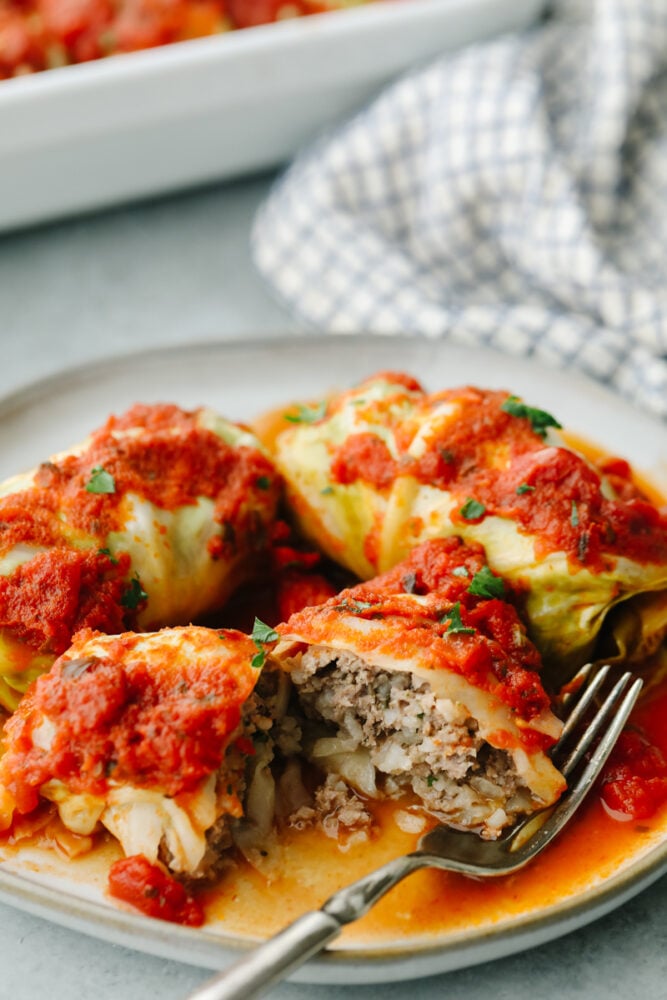 These stuffed cabbage rolls are SOO GOOD! These are packed with lean ground beef, onion, garlic, dill, and just a hint of nutmeg. The cabbage rolls are slow-cooked in marinara sauce until they're melt-in-your-mouth delicious! A cabbage roll on a plate with a fork cutting into one.