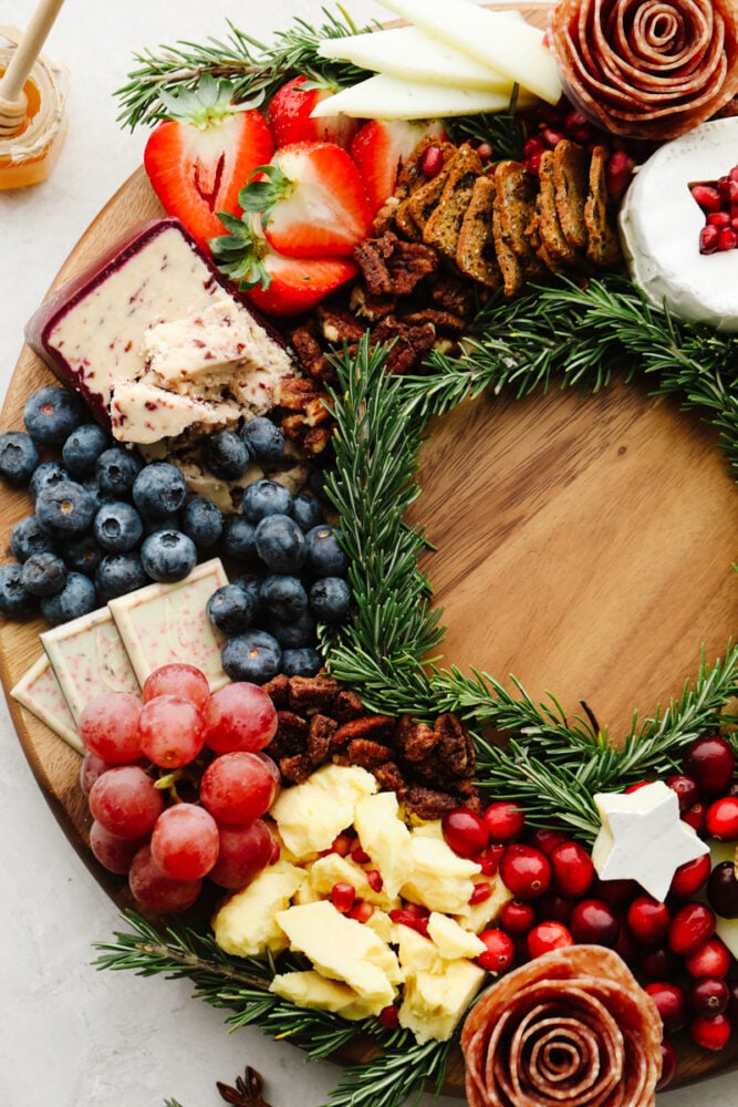 This Christmas wreath charcuterie board is the perfect festive touch to any holiday party! It's stunning and delicious! Plus, it's super easy to make and all of your guests will be so impressed! A close up of the side of the Christmas wreath charcuterie board. Grapes, cheese, pecans, cranberries and blueberries.