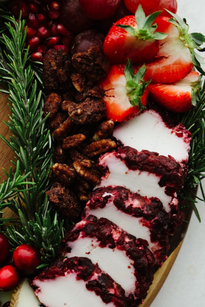 This Christmas wreath charcuterie board is the perfect festive touch to any holiday party! It's stunning and delicious! Plus, it's super easy to make and all of your guests will be so impressed! A close up of some cheese, candied pecans, strawberries and a rosemary sprig.