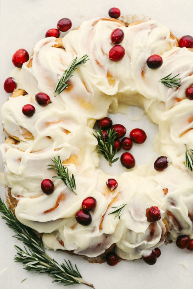 The holiday season doesn't get much more festive at the dinner table than with this cinnamon roll wreath! It's beautiful and delicious which makes it the perfect choice for your holiday breakfast, brunch, or dessert! A cinnamon roll wreath with berries and garnish.