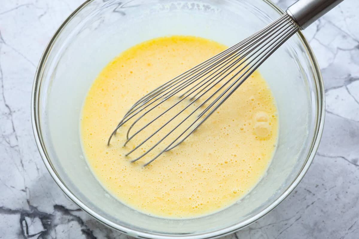 Corn pudding is creamy, slightly sweet, with a hint of savory! It's packed with cream, butter, sweet and juicy corn kernels, all baked to perfection. It will be an awesome addition to your Thanksgiving spread, or make it for any weeknight. Overhead shot of eggs whisked in a glass bowl.