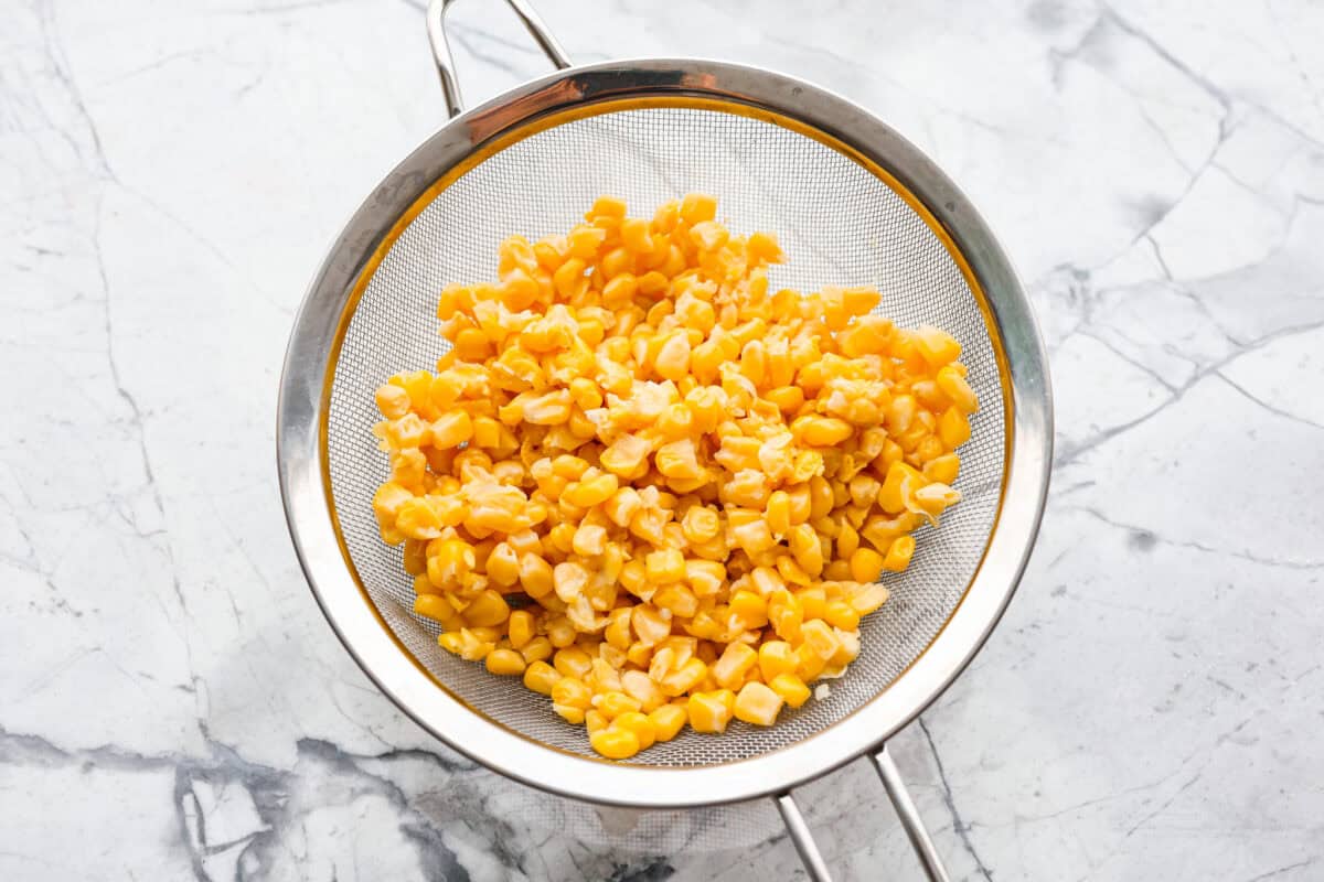 Corn pudding is creamy, slightly sweet, with a hint of savory! It's packed with cream, butter, sweet and juicy corn kernels, all baked to perfection. It will be an awesome addition to your Thanksgiving spread, or make it for any weeknight. Overhead shot of drained corn in a strainer.