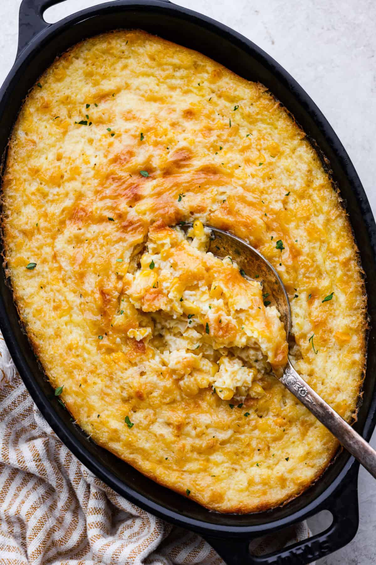 Corn pudding is creamy, slightly sweet, with a hint of savory! It's packed with cream, butter, sweet and juicy corn kernels, all baked to perfection. It will be an awesome addition to your Thanksgiving spread, or make it for any weeknight. Overhead shot of corn pudding in a baking dish with a serving spoon in it.