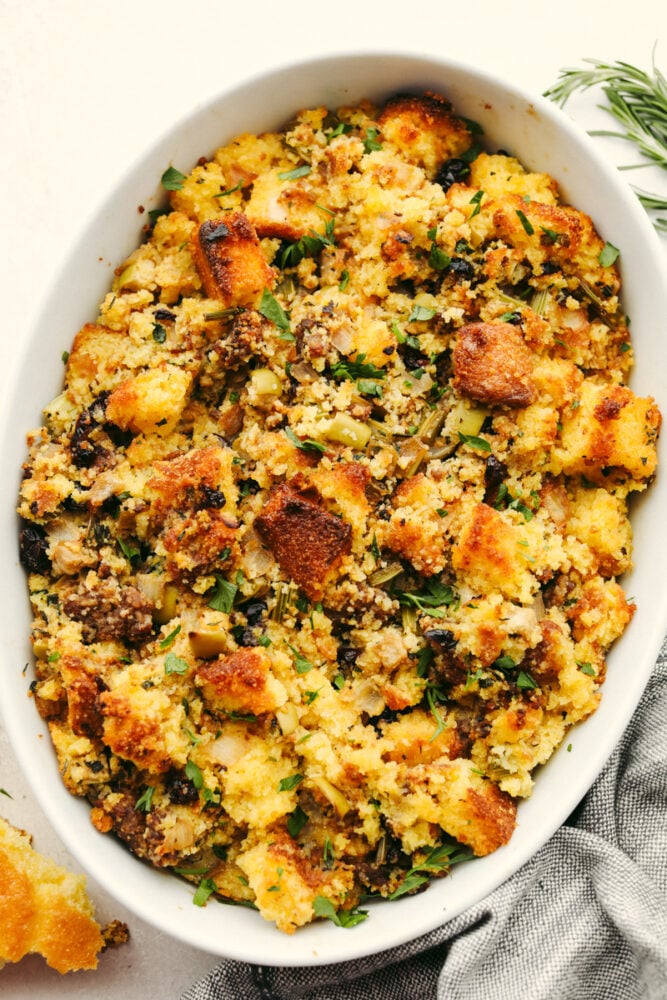 Cornbread stuffing is a delicious hearty dish that your family will go crazy over this Thanksgiving! It's loaded with fresh herbs, fruits, and veggies for the perfect sweet and savory side. Cornbread stuffing in a white casserole dish.