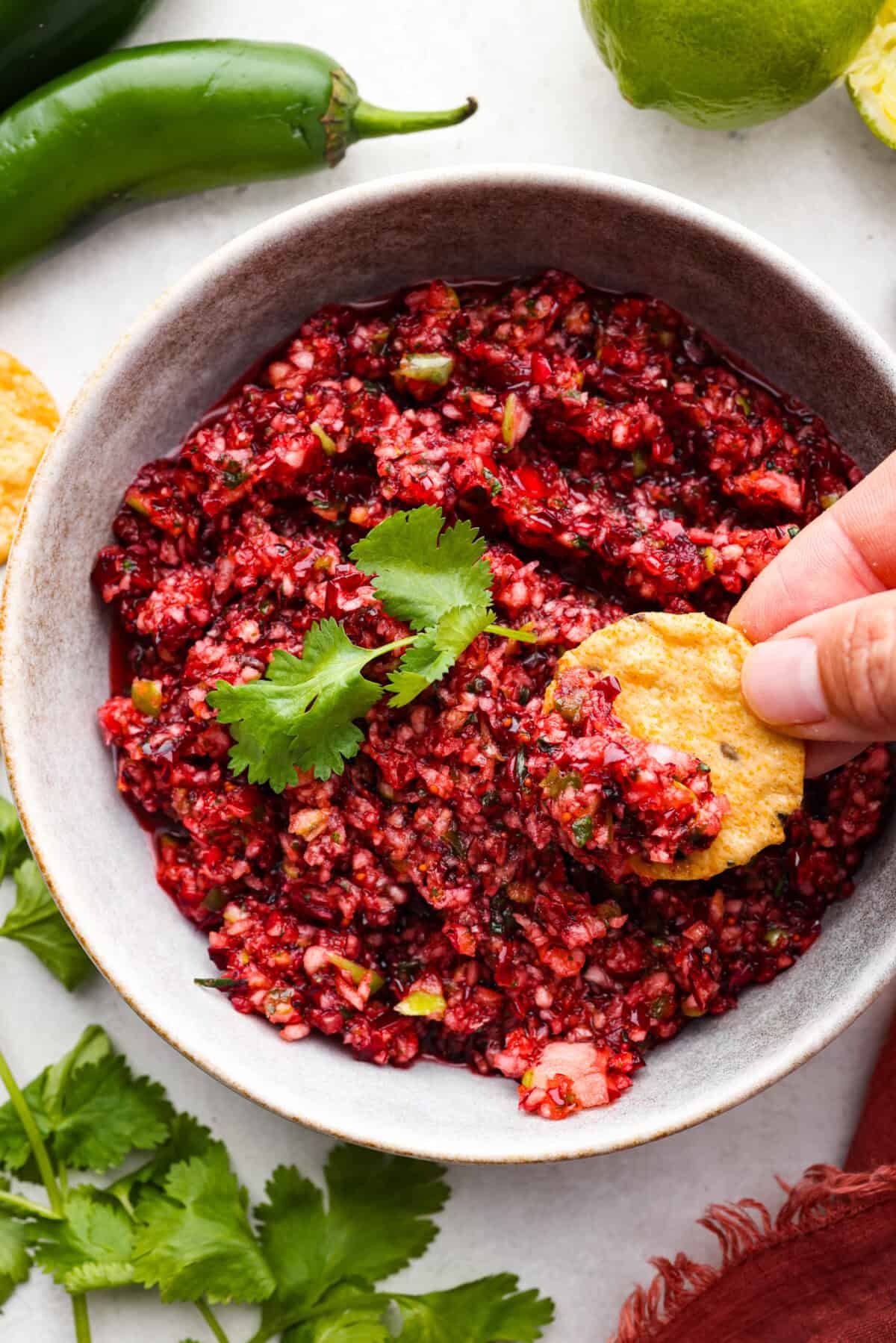 Cranberry salsaย is a fresh cranberry mixture of sweet and savory that is laid over cream cheese. It makes for the BEST holiday appetizer! You can also serve it in place of cranberry sauce with your Thanksgiving dinner. Overhead shot of someone scooping a bite of salsa onto a chip.