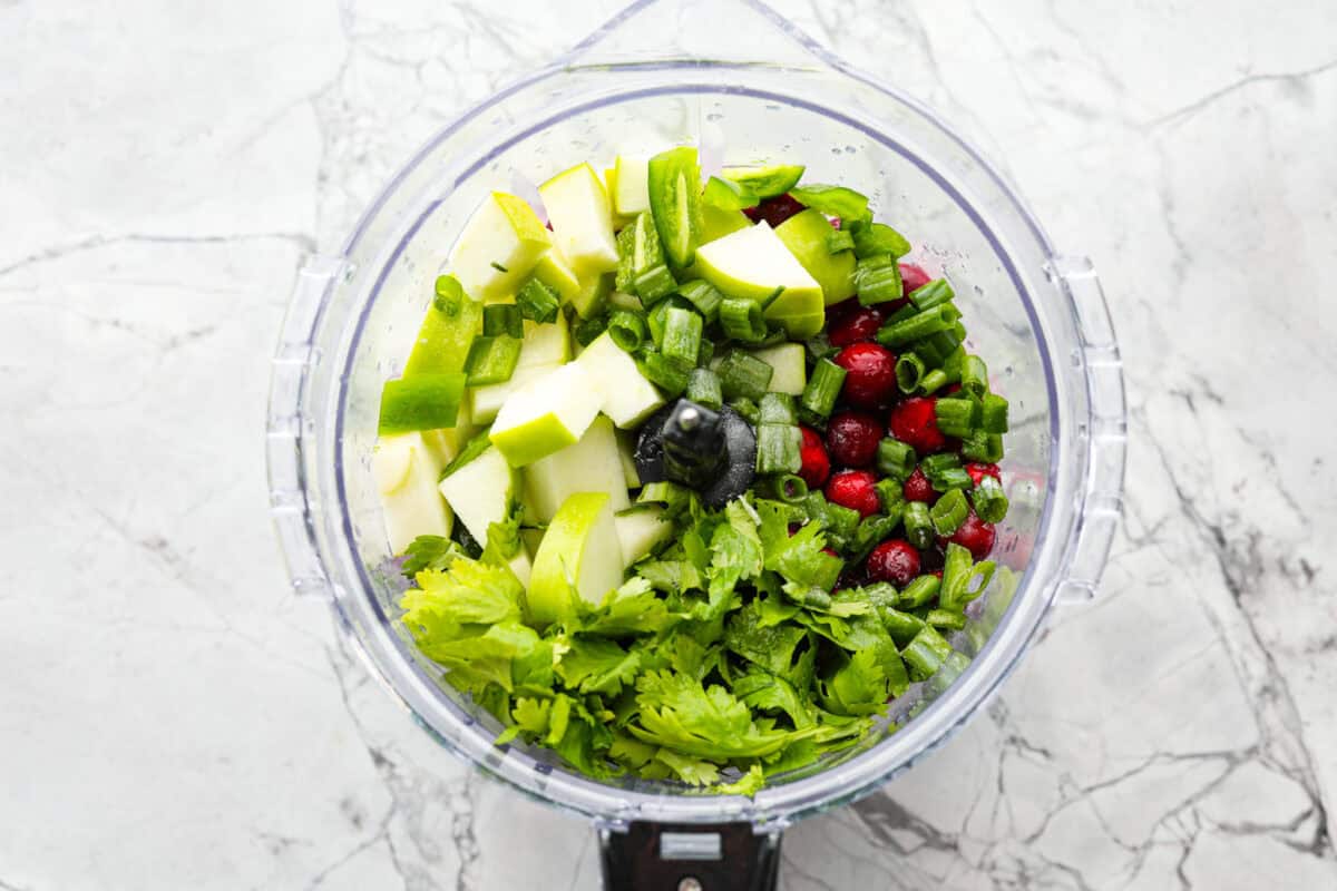 Cranberry salsaย is a fresh cranberry mixture of sweet and savory that is laid over cream cheese. It makes for the BEST holiday appetizer! You can also serve it in place of cranberry sauce with your Thanksgiving dinner. Overhead shot of ingredients in a food processor.