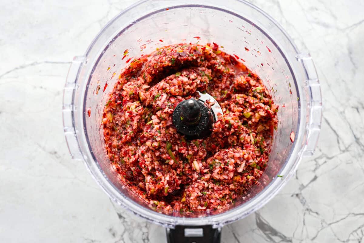 Cranberry salsaย is a fresh cranberry mixture of sweet and savory that is laid over cream cheese. It makes for the BEST holiday appetizer! You can also serve it in place of cranberry sauce with your Thanksgiving dinner. Overhead shot of ingredients mixed in a food processor.