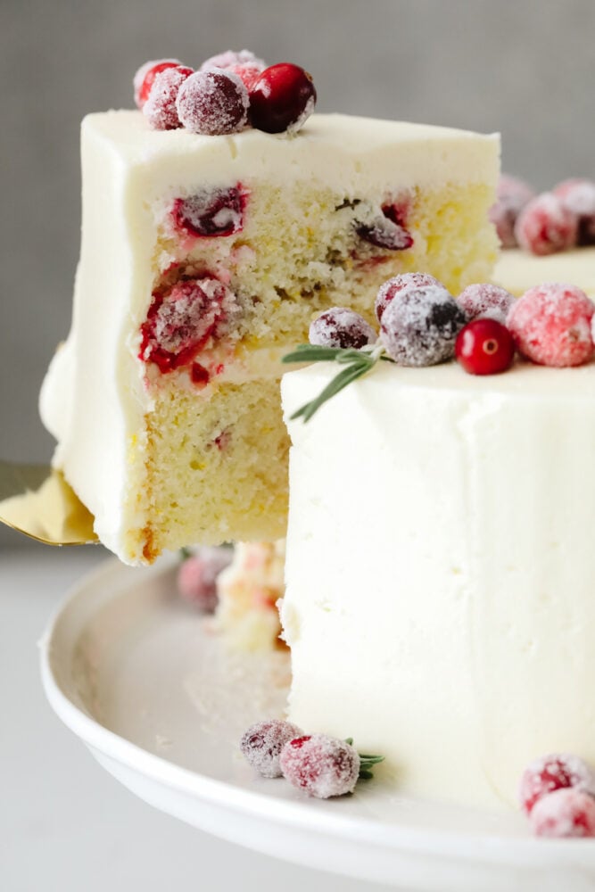 Cranberry Christmas cake is a show-stopping dessert you've got to try this holiday season! It's an amazing white cake filled with cranberries and topped with indulgent white chocolate buttercream! Taking a slice of cake.