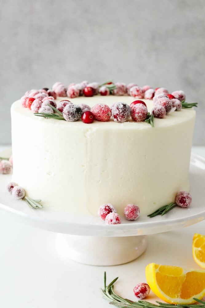 Cranberry Christmas cake is a show-stopping dessert you've got to try this holiday season! It's an amazing white cake filled with cranberries and topped with indulgent white chocolate buttercream! A full frosted cake topped with cranberries dusted in sugar.