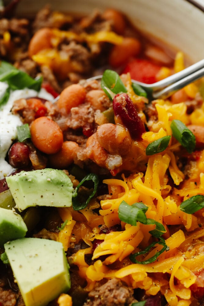 Crockpot chili is the ultimate comfort food! This chili is SO easy and insanely good that everyone will come back for seconds! A close up of chili with a spoon scooping some out of a bowl.