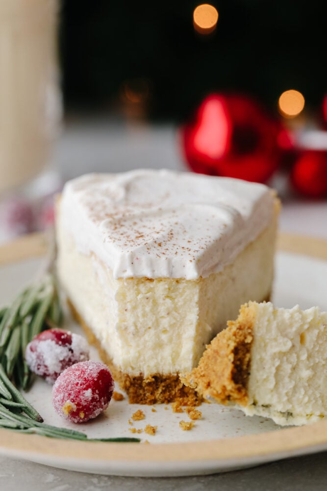 This eggnog cheesecake is SOO GOOD. It's creamy and melts in your mouth! That classic eggnog taste makes it the best dessert for the holiday season! A slice of cheesecake with a fork cutting into it.