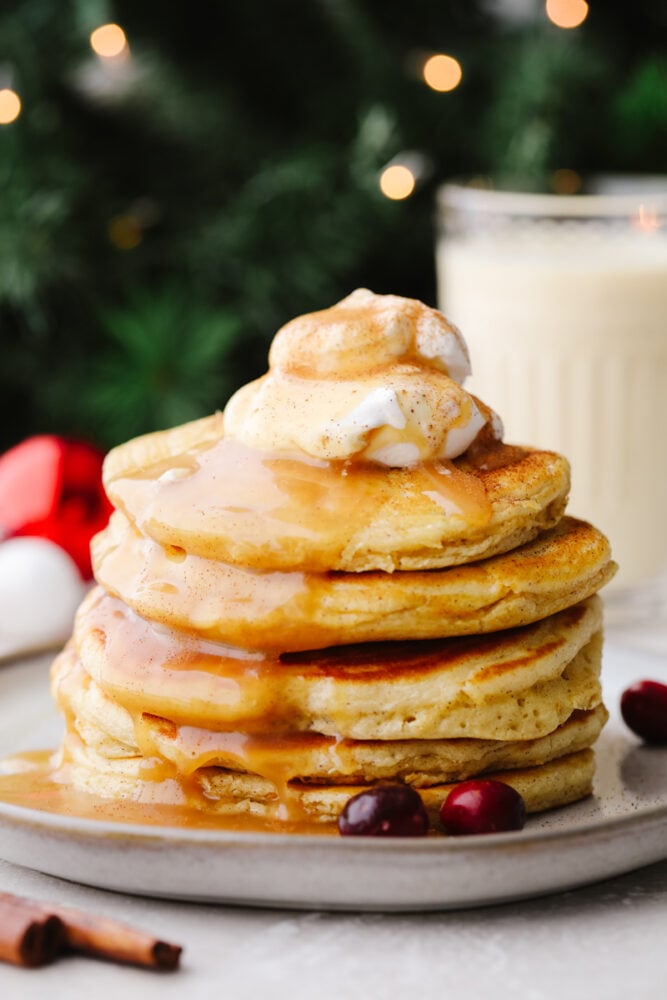 These eggnog pancakes are a MUST TRY this holiday season! They are soft and sweet and will melt right in your mouth. The hint of eggnog will have everyone coming back for more! A stack of eggnog pancakes with caramel sauce and whipped cream.