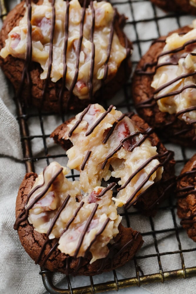 German chocolate cookies are classic and delicious! This chocolate cookie has a coconut and pecan topping that is drizzled with chocolate. It's perfect for any occasion! A German chocolate cookie broken in half on a cooling rack.