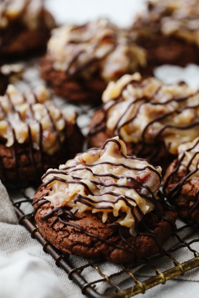 German chocolate cookies are classic and delicious! This chocolate cookie has a coconut and pecan topping that is drizzled with chocolate. It's perfect for any occasion! A zoomed in shot of German chocolate cookies on a cooling rack.