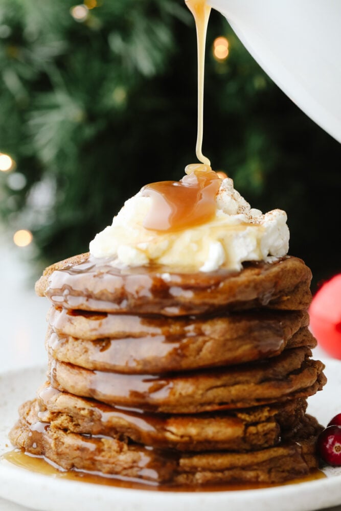 Add holiday spice to your breakfast with these amazing gingerbread pancakes! Soft, fluffy, and drizzled in a homemade caramel sauce, this is a treat you won't want to pass up! A stack of gingerbread pancakes being drizzled in caramel.