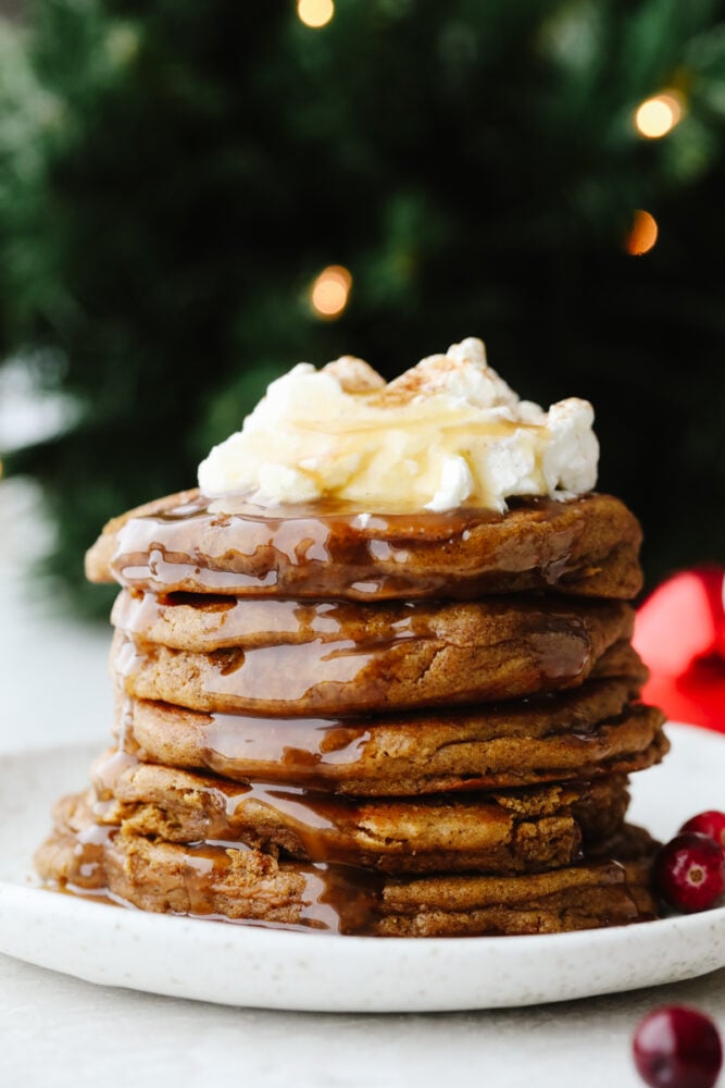 Add holiday spice to your breakfast with these amazing gingerbread pancakes! Soft, fluffy, and drizzled in a homemade caramel sauce, this is a treat you won't want to pass up! A stack of gingerbread pancakes topped with whipped cream and caramel sauce.