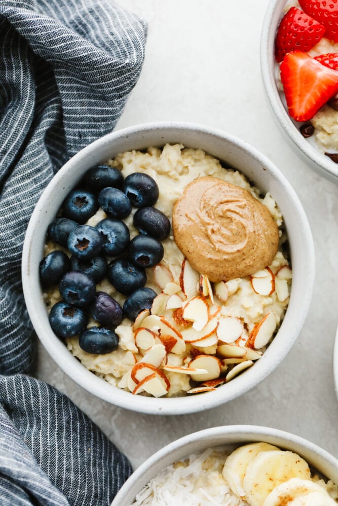 A warm, tasty bowl of homemade oatmeal is the perfect way to start your day! Here are 4 yummy variations filled with fresh fruit, nuts, brown sugar, and more! A bowl of oatmeal topped with almond slices, peanut butter, and blueberries.