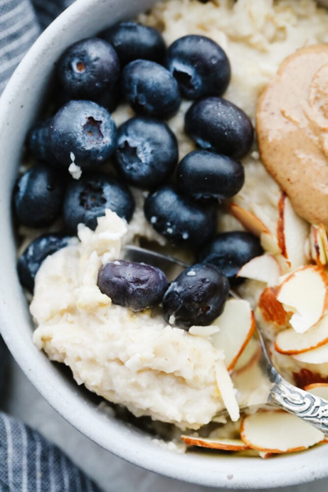 A warm, tasty bowl of homemade oatmeal is the perfect way to start your day! Here are 4 yummy variations filled with fresh fruit, nuts, brown sugar, and more! A closeup of oatmeal topped with blueberries, almonds, and nut butter.
