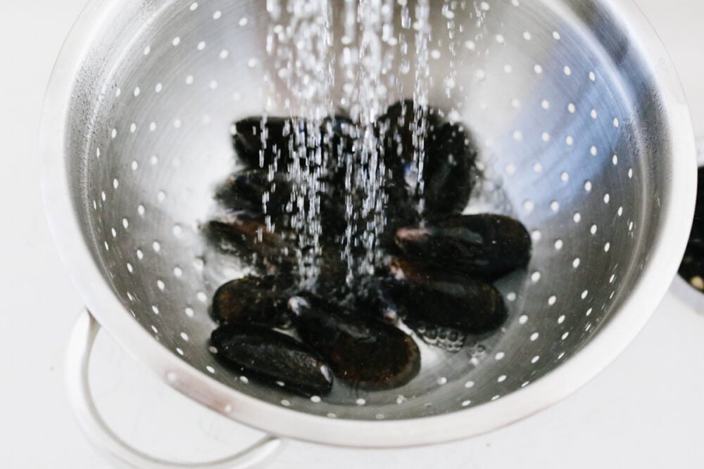 These steamed mussels are easy, elegant, and delicious! They are perfect for any dinner party and you won't be able to stop after just one! Mussels being rinsed with water.