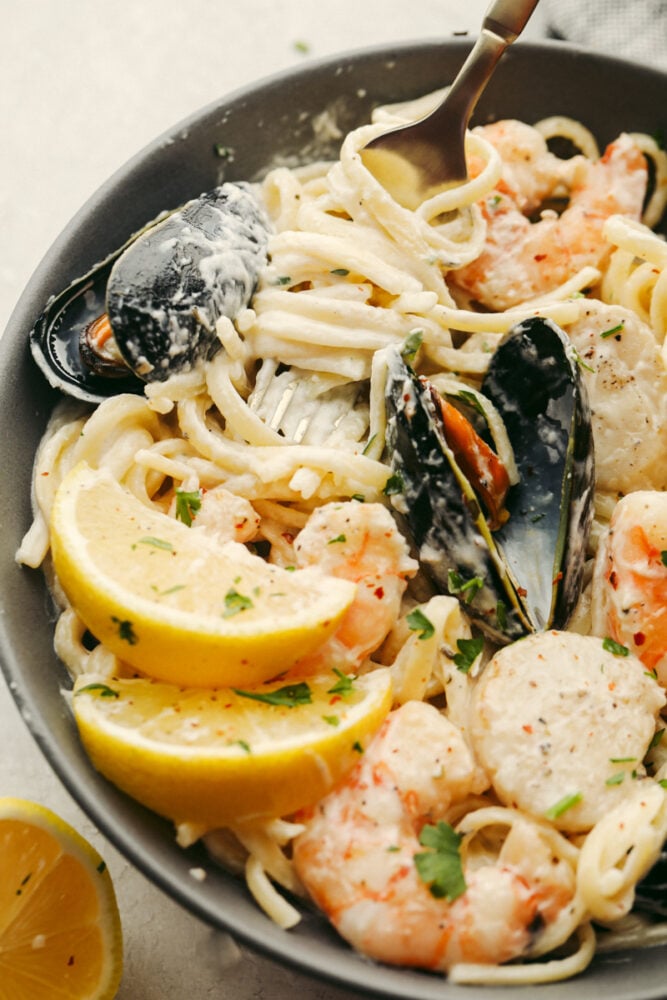 My seafood pasta has a silky lemon garlic cream sauce that is to die for! It's loaded with tender shrimp, scallops, and mussels. Itโs the perfect date night dish! Seafood pasta in a bowl with a fork in the bowl.