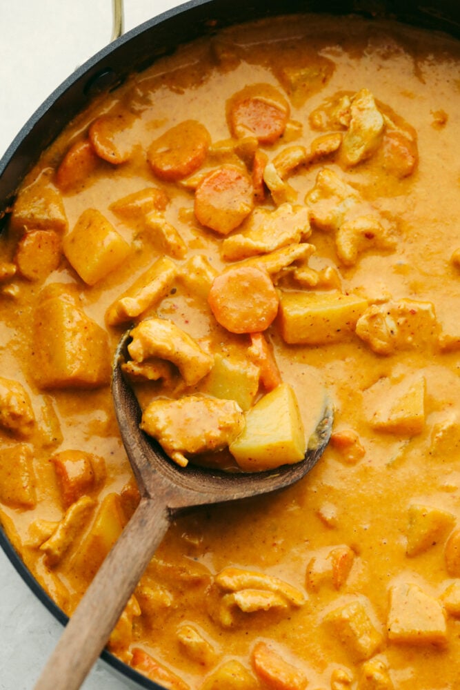 This massaman curry is insanely delicious!! Tender and juicy chicken mixed with a creamy blend of flavors gives it the best taste that ALL of your guests will love!! Massaman curry in a pan being scooped with a wooden spoon.