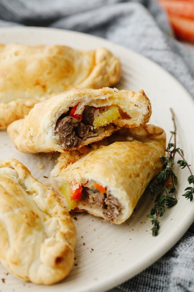 These traditional English cornish pasties are SOO GOOD! The outside is a flaky crust that's filled with delicious steak, potatoes and veggies! If you haven't tried this before then you are in for a real treat! Cornish pasties on a plate cut open so that you can see the meat and veggies inside.