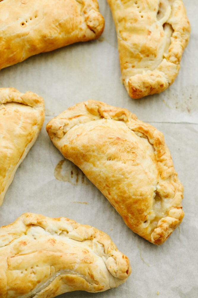 These traditional English cornish pasties are SOO GOOD! The outside is a flaky crust that's filled with delicious steak, potatoes and veggies! If you haven't tried this before then you are in for a real treat! Cornish pasties cooked and on a pan with parchment paper.