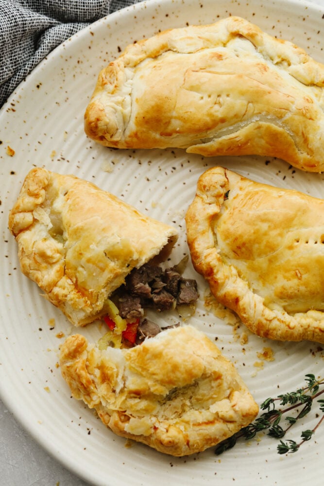 These traditional English cornish pasties are SOO GOOD! The outside is a flaky crust that's filled with delicious steak, potatoes and veggies! If you haven't tried this before then you are in for a real treat! A few cornish pasties on a plate. One has been cut open.