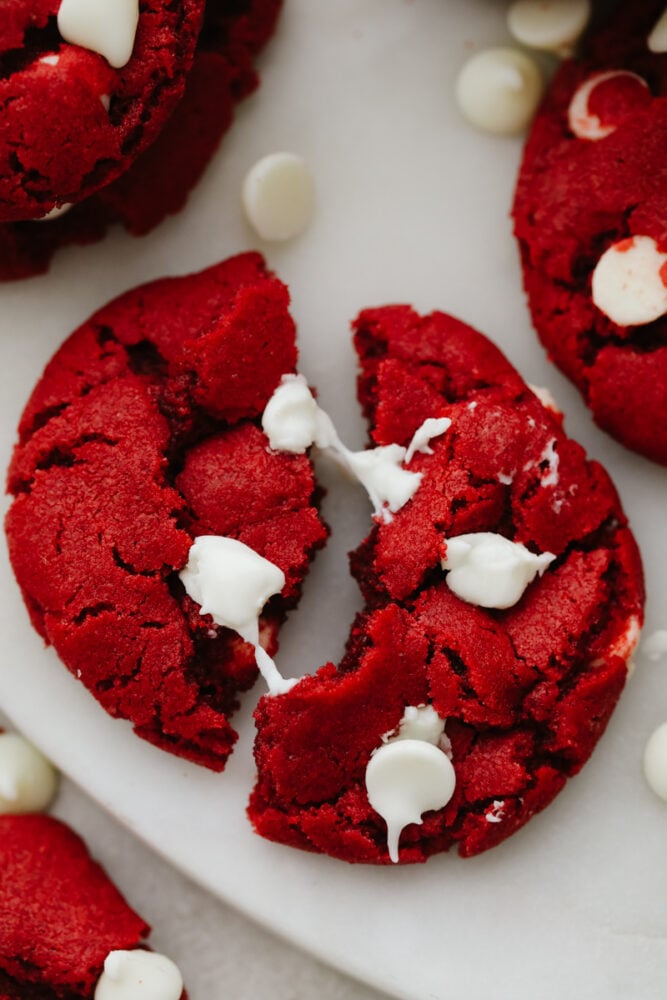 Delicious and chewy red velvet cookies with white chocolate chips. Rich, sweet, with a hint of tang, this is the dessert you'll be needing for all of your holiday parties! Closeup of a cookie broken into 2 pieces.