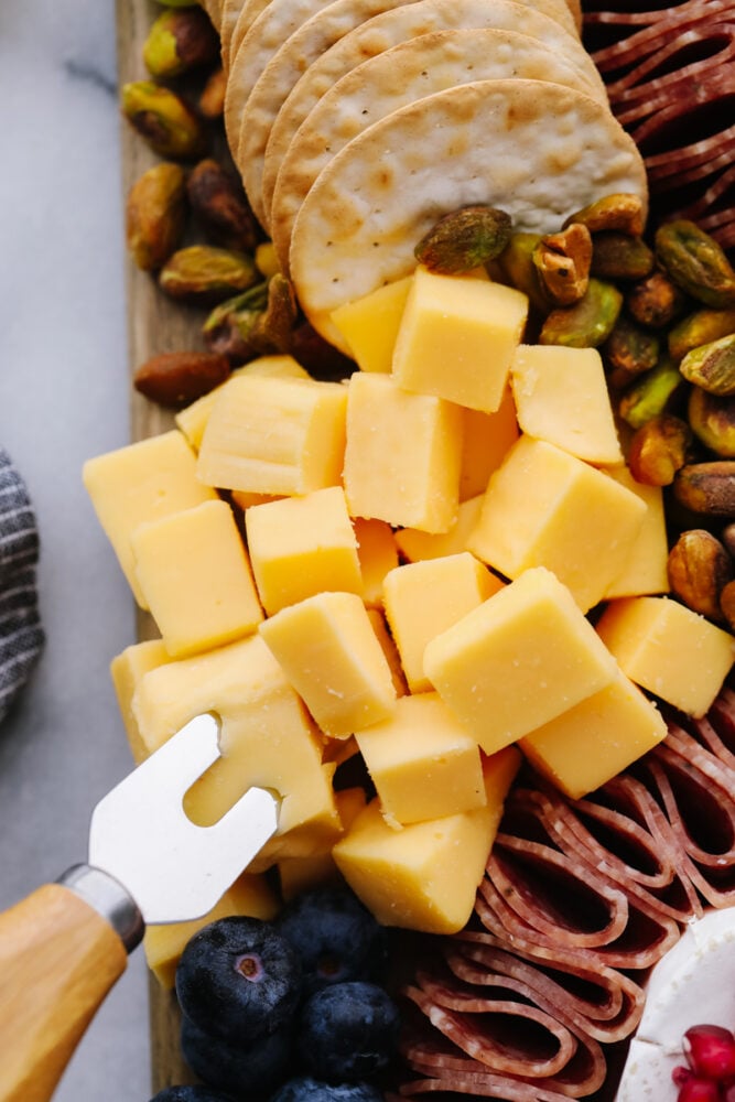 A simple charcuterie board is all that you need for any holiday or event! Filled with all of your favorite things, it will for sure be the star of the show! A zoomed in picture of cheese, salami and blueberries.