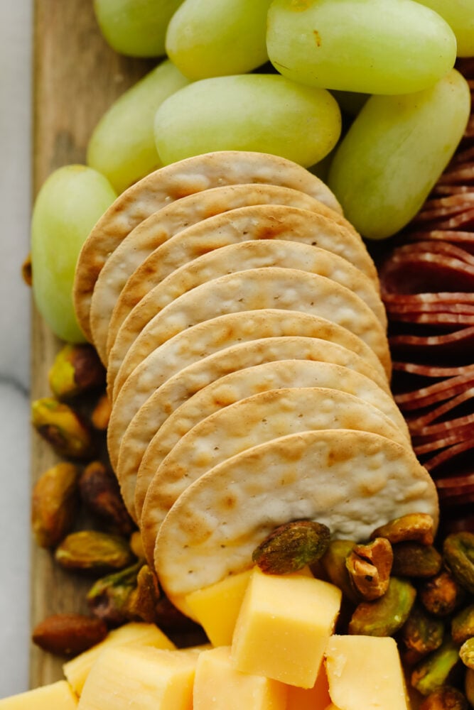 A simple charcuterie board is all that you need for any holiday or event! Filled with all of your favorite things, it will for sure be the star of the show! A picture of crackers and pistachios on a charcuterie board.