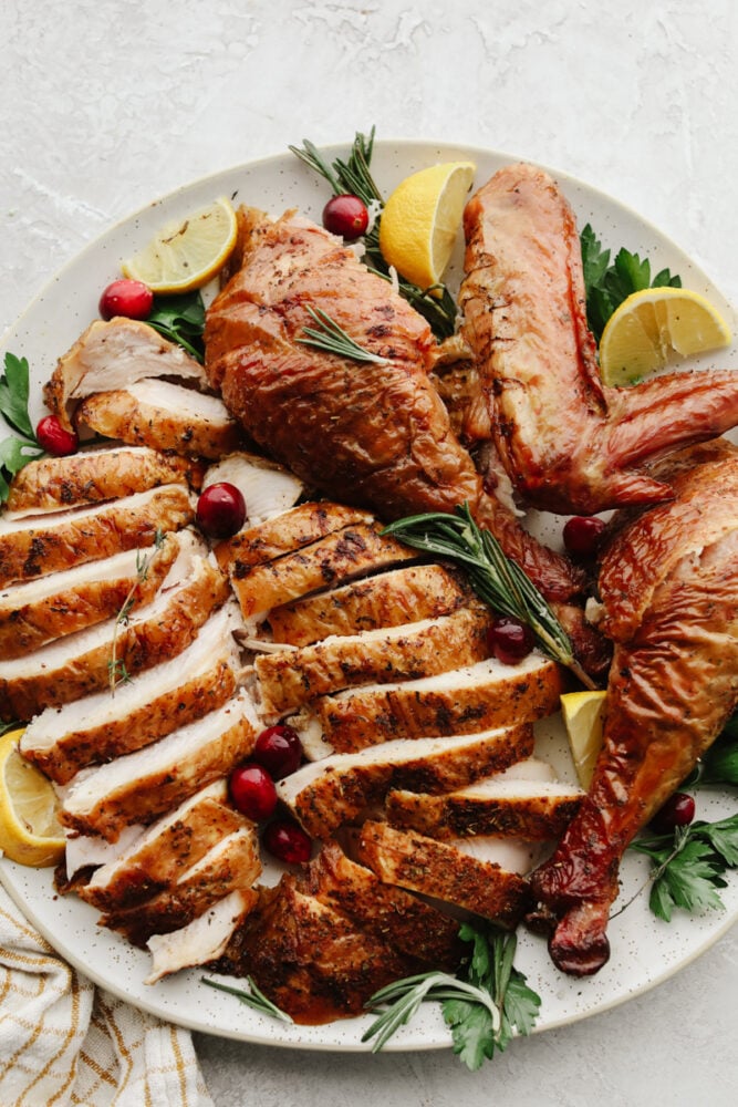 Just in time for Thanksgiving, this perfect smoked turkey is juicy and tender with a subtle smoky flavor. A simple brine and fresh herbs make each bite burst with flavor! Sliced turkey on a white plate with rosemary, lemon, and cranberry garnish.