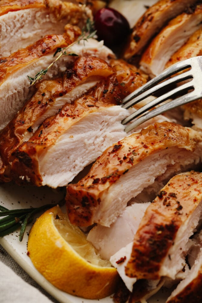 Just in time for Thanksgiving, this perfect smoked turkey is juicy and tender with a subtle smoky flavor. A simple brine and fresh herbs make each bite burst with flavor! Closeup of a slice being stuck with a fork.