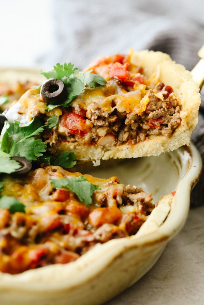 This taco pie is the ultimate Mexican casserole! It's a seasoned homemade crust filled with taco meat, cheese, beans, and tomatoes. It's a MUST TRY recipe for sure! A slice of taco pie being taken out of the pan.