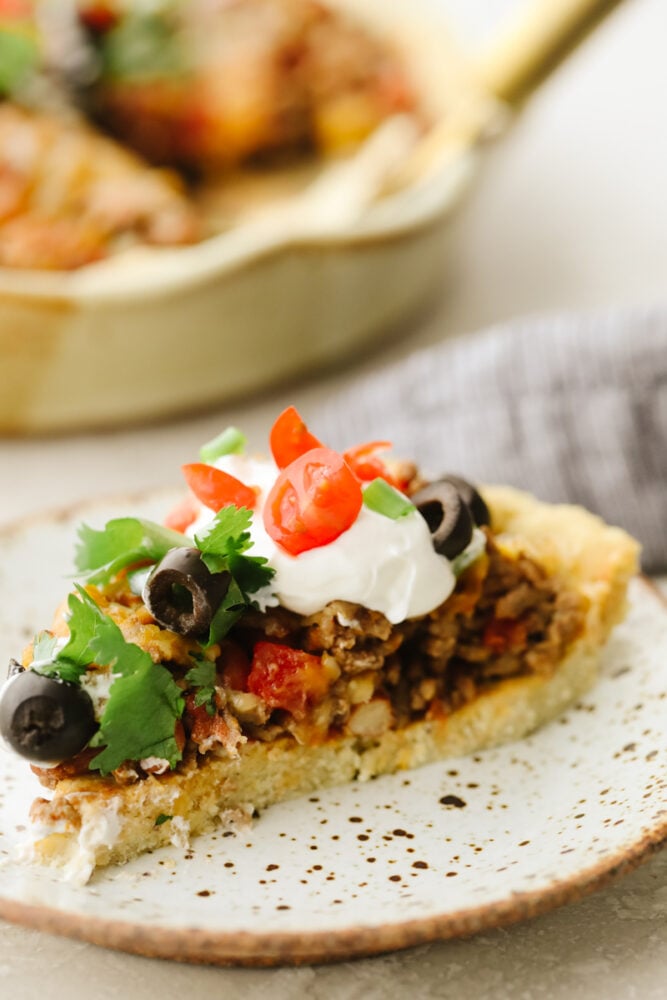 This taco pie is the ultimate Mexican casserole! It's a seasoned homemade crust filled with taco meat, cheese, beans, and tomatoes. It's a MUST TRY recipe for sure! A slice of pie on a plate with toppings.