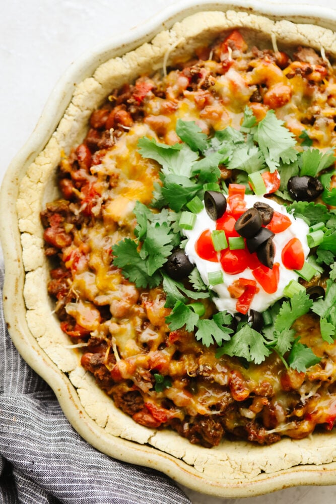 This taco pie is the ultimate Mexican casserole! It's a seasoned homemade crust filled with taco meat, cheese, beans, and tomatoes. It's a MUST TRY recipe for sure! A taco pie garnished with toppings.