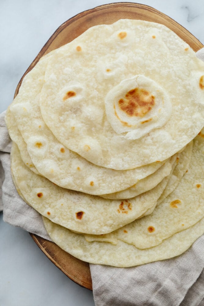These homemade tortillas not only taste amazing but they are simple and easy to make. They will knock your socks off and take any recipe to the next level! A stack of homemade tortillas on a platter.