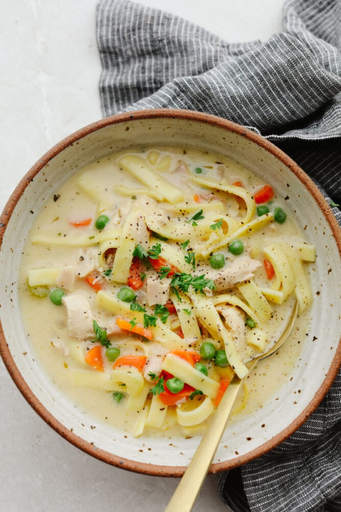 Making a big pot of turkey noodle soup is the best way to use up your Thanksgiving leftovers! Itโs creamy, savory, and filled with delicious herbs and veggies! Your family is going to love this easy, hearty meal. Turkey noodle soup served in a stoneware bowl.
