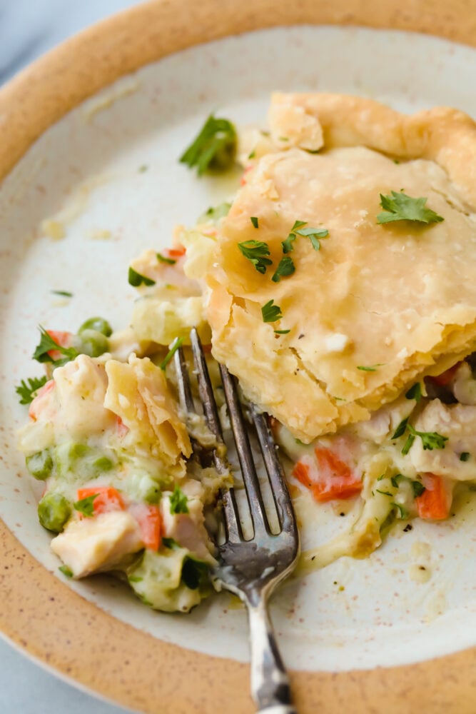 This turkey pot pie is a hearty and classic dinner! It has a flakey crust and a creamy, vegetable and turkey filling that your entire family will go crazy over! Turkey pot pie on a plate with a fork cutting into it.