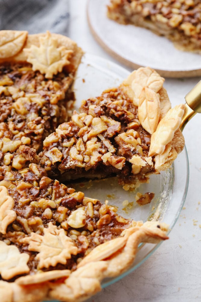 This sweet and nutty walnut pie is the perfect dessert for all of your holiday parties. There are flavors of caramelized brown sugar and butter running throughout, making each bite a dream! Taking a slice of walnut pie out of the pan.