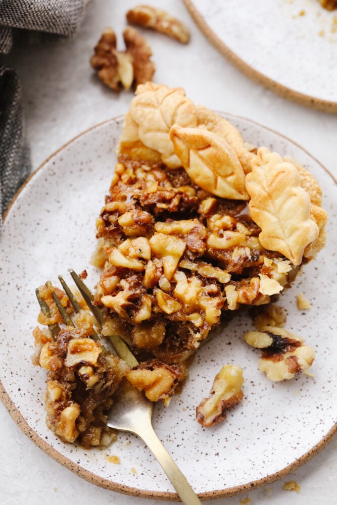 This sweet and nutty walnut pie is the perfect dessert for all of your holiday parties. There are flavors of caramelized brown sugar and butter running throughout, making each bite a dream! Taking a bite of a walnut pie slice.