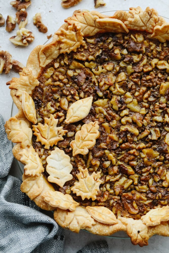This sweet and nutty walnut pie is the perfect dessert for all of your holiday parties. There are flavors of caramelized brown sugar and butter running throughout, making each bite a dream! A walnut pie topped with leaf-shaped crust pieces.