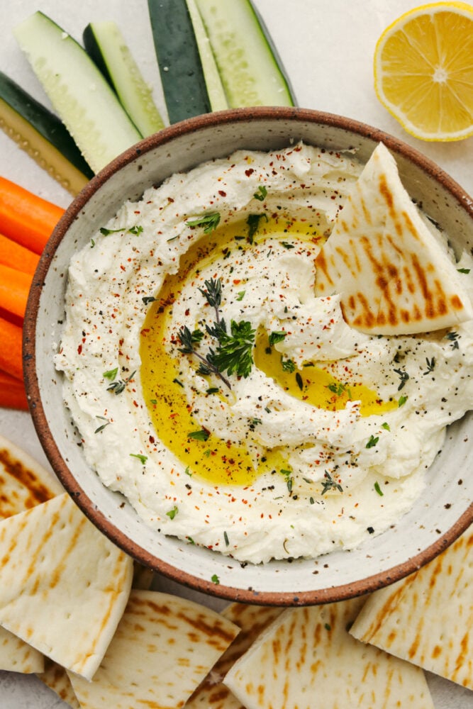 It doesn't get much better than whipped feta dip!! Perfectly creamy and garnished with herbs and spices, this dip will be the talk of the party! Whipped feta dip in a bowl with a pita slice in it.